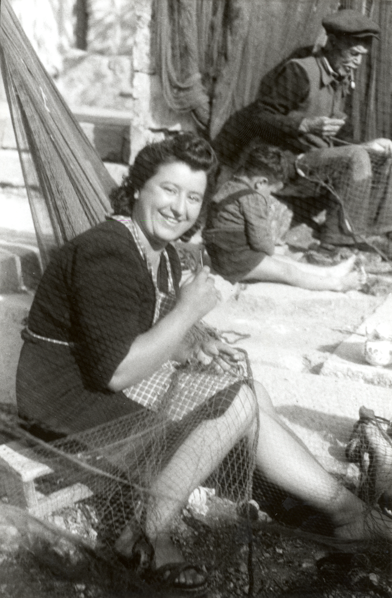 Post-WWII, Mrs Vida and the fisherman Josip of the “Živčevi” family busy mending fishing nets in Santa Croce (Trieste, Italy)